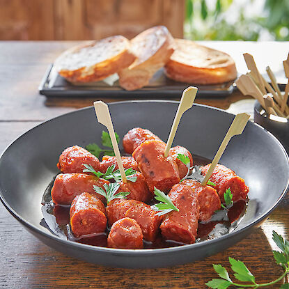 Bol noir avec chorizo tapas à l’huile, piques en bois et persil, pain grillé à l’arrière-plan sur un plateau.