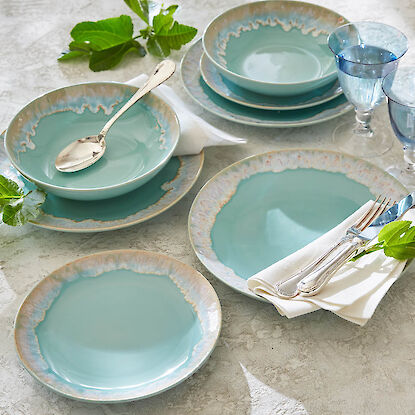 Vaisselle en céramique turquoise avec assiettes et bols, couverts et verres, présentée sur une table claire.