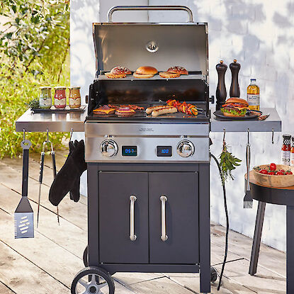 Barbecue à gaz avec affichage numérique, viandes et légumes grillés, accessoires et sauces à côté.