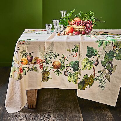 Tisch mit Obst und Gläsern, dekoriert mit einer bestickten Tischdecke mit Früchtemotiven.