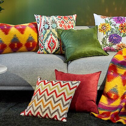 graues sofa mit vielen bunten kissen beistel tisch und bunter decke