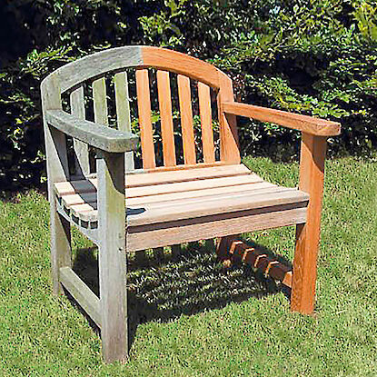 Banc de jardin en bois à moitié nettoyé, posé sur une pelouse devant une haie – la différence entre le bois vieilli et restauré est clairement visible.