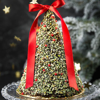 Sapin de Noël en chocolat 3D sur une assiette en verre devant un sapin.