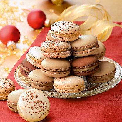 Macarons de Noël garnis sur une nappe rouge, avec des boules de Noël rouges en arrière-plan.