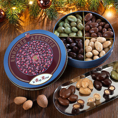 Amandes provençales grillées dans un petit bol bleu, posées sur une table brune avec des branches de sapin en arrière-plan.