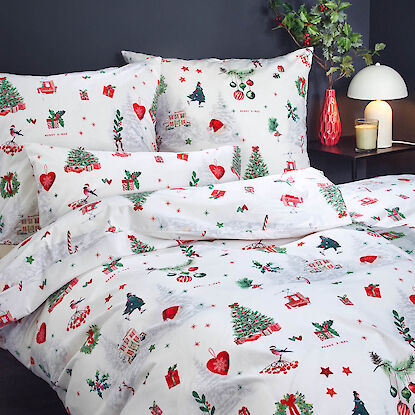 Festliche Bettwäsche in Weiß mit roten und grünen Weihnachtsmotiven, dekoriert mit Kissen und Tannenzweigen