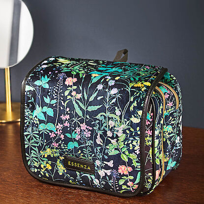 Kosmetiktasche Essenza in schwarzem Stoff mit buntem Blumenprint auf einer Holzkommode