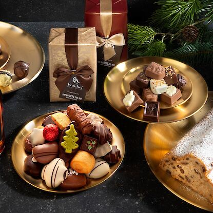 Festliche Pralinen, Likör und Stollen auf goldenen Tellern mit Champagnerflasche und Tannenzweigen