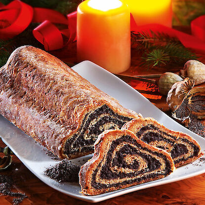 Aufgeschnittener Mohnstollen auf weißer Platte mit brennenden Kerzen und weihnachtlicher Deko