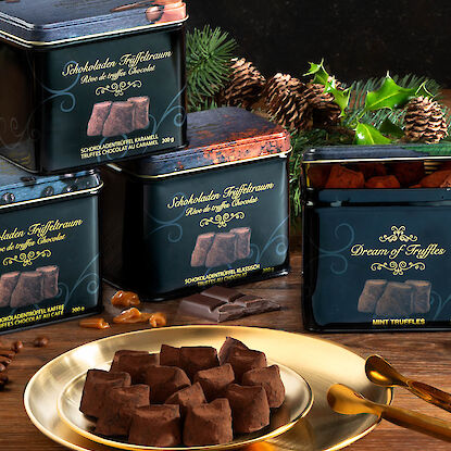 Edle Schokoladentrüffel in dekorativen Dosen mit goldener Platte und weihnachtlicher Dekoration