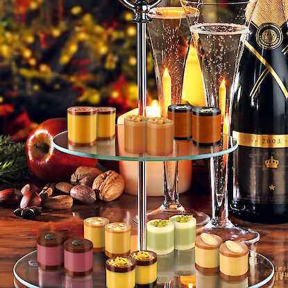 Kleine Dessertpralinen auf Etagere mit Sektgläsern, Nüssen und festlicher Beleuchtung