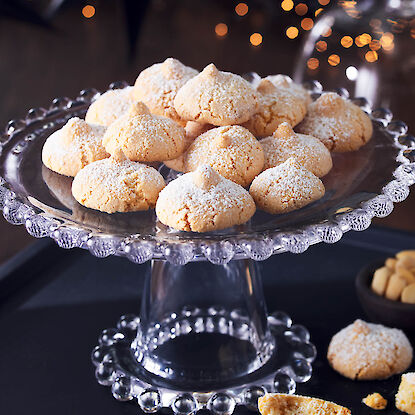 Helles Amaretti-Gebäck auf gläserner Tortenplatte mit Puderzucker und Bokeh-Licht
