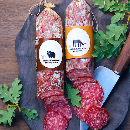 Zwei Salamis, Wildschwein und Hirsch, auf Holzbrett mit Eichenblättern und Messer