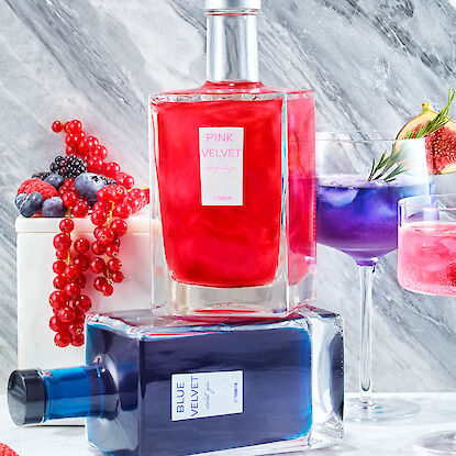Flaschen Pink Velvet und Blue Velvet Gin mit Beeren und Cocktails auf Marmor