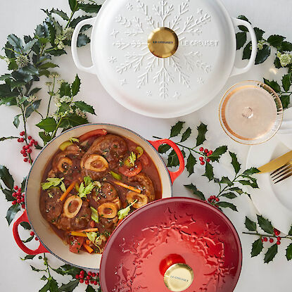 Weißer und roter Le Creuset Schmortopf mit Osso Buco, festlich mit Stechpalmen dekoriert