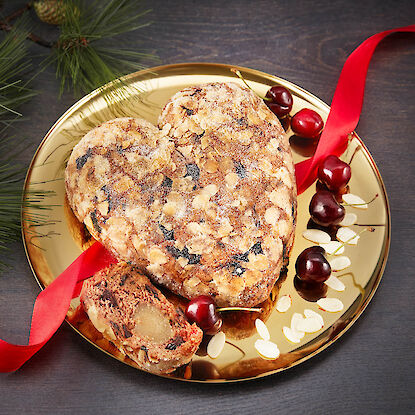 Herzförmiger Stollen mit Mandeln, Kirschen und rotem Band auf goldenem Teller serviert