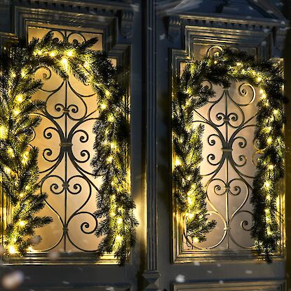 Beleuchtete Tannengirlanden rahmen festlich verzierte Fenster im winterlichen Abendlicht