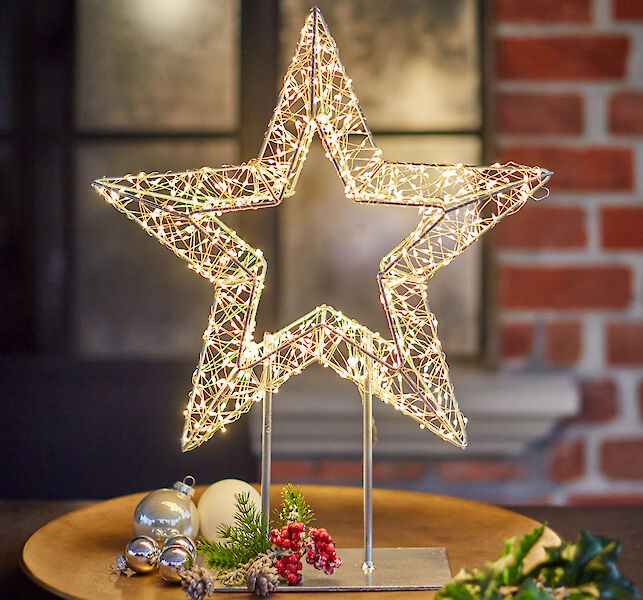 Beleuchteter Drahtstern mit Weihnachtsdeko und Tannenzweigen auf Holztisch
