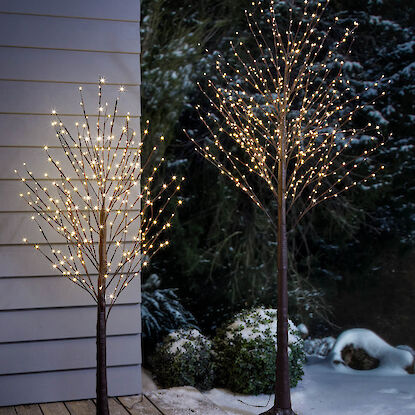 Zwei leuchtende LED-Bäume im verschneiten Garten auf Holzterrasse