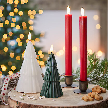 Tannenbaum- und Stabkerzen in Rot, Grün und Weiß auf Holzteller mit Weihnachtsdeko