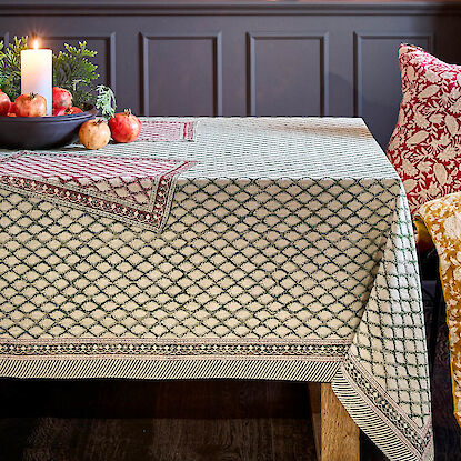 Festlich gedeckter Tisch mit gemusterter Tischdecke, Kerze und Granatäpfeln als Dekoration