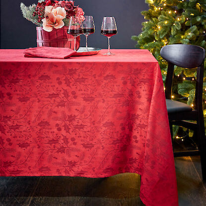 Rote Tischdecke mit Blumenarrangement, Rotwein und Weihnachtsbaum im Hintergrund