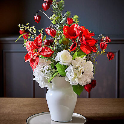 Festlicher Strauß mit roten und weißen Blumen in weißer Vase auf Holztisch