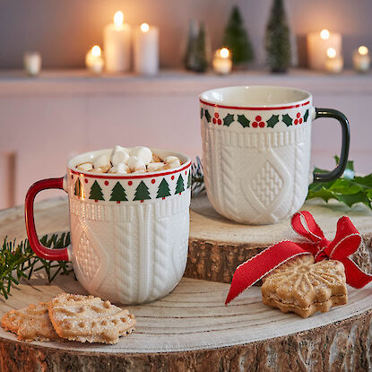 Zwei Weihnachtstassen mit Kakao, Marshmallows und Gebäck auf Holzscheibe