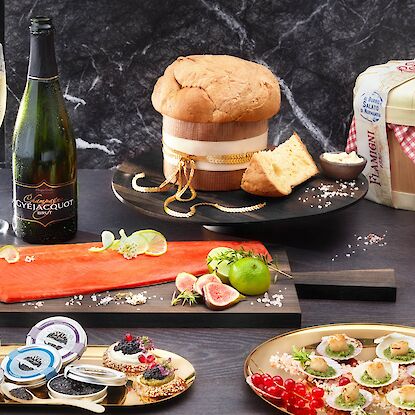 Edle Festtagsdelikatessen mit Kaviar, Lachs, Champagner und Panettone – luxuriös angerichtet auf dunklem Tisch