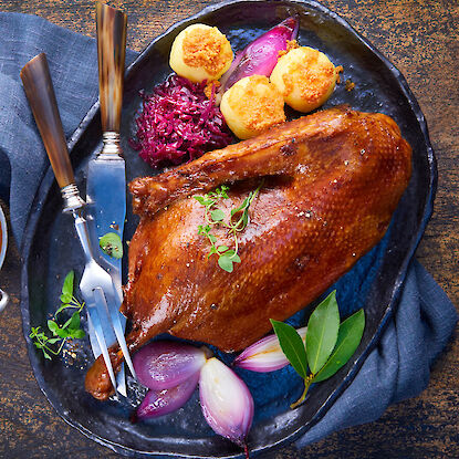 Knusprige Festtagsente mit Rotkohl, Zwiebeln und Klößen – klassisches Weihnachtsgericht auf schwarzer Platte