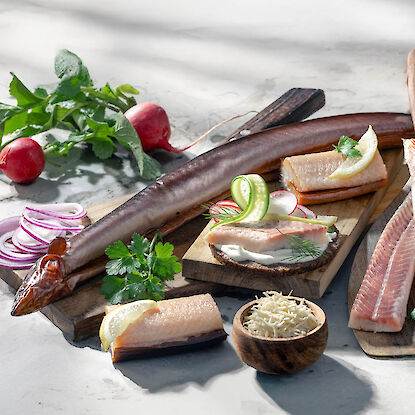Geräucherter Fisch auf Holzbrett – Aal, Forelle und Meerrettich mit frischen Kräutern und Radieschen