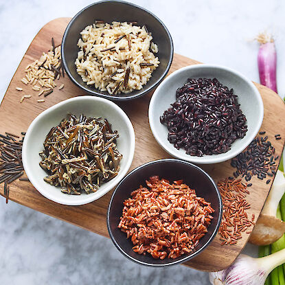 Bunte Reissorten in Schalen – schwarzer, roter, Wild- und Naturreis dekorativ auf Holzbrett angerichtet