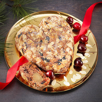 Früchtebrot in Herzform mit Mandeln und Kirschen auf goldener Platte – festliches Gebäck zu Weihnachten