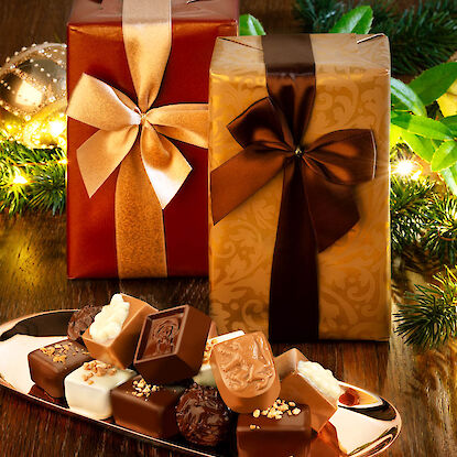 Pralinenmischung auf goldener Platte mit festlich verpackten Geschenken – edle Schokolade für Weihnachten