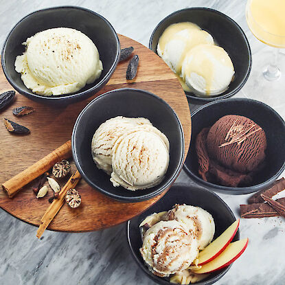 Verschiedene Eissorten in schwarzen Schalen mit Gewürzen, Schokolade und Apfelscheiben
