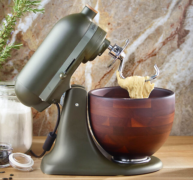 Grüne Küchenmaschine mit Holzmischschüssel knetet Teig auf Holzarbeitsplatte.