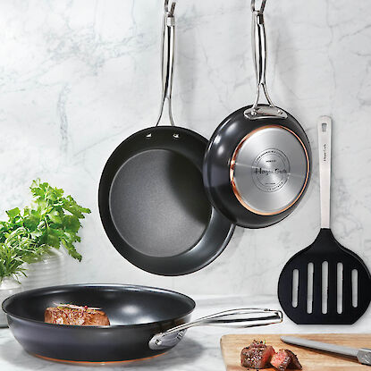 Drei edle Hagen Grote Pfannen mit Edelstahlgriffen hängen in moderner Küche.