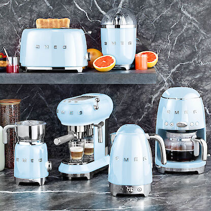 Hellblaue Smeg Küchengeräte wie Toaster, Espressomaschine und Wasserkocher auf Marmortheke.