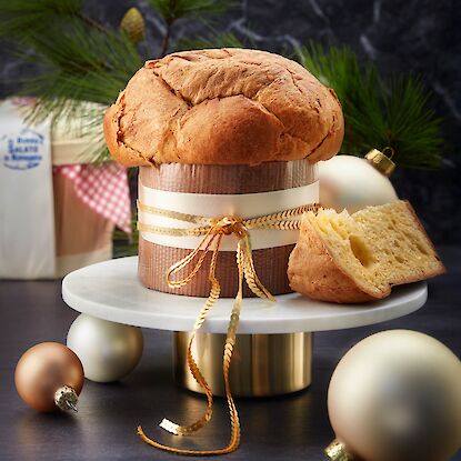 Traditioneller Panettone auf Marmorteller mit Weihnachtskugeln und Tannenzweigen dekoriert.