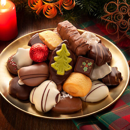 Weihnachtliches Gebäck und Pralinen auf goldener Platte mit Kerze und Tannendeko.