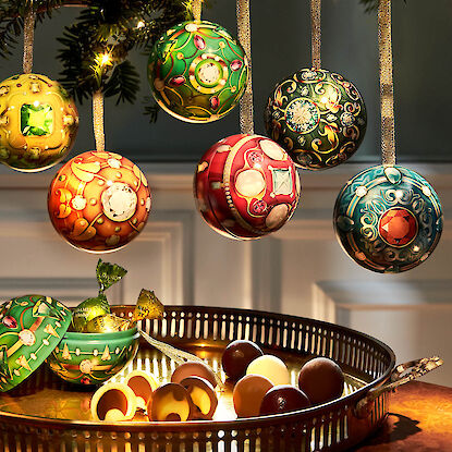 Bunte Schmuckdosen in Kugelform mit Pralinen und Weihnachtsbeleuchtung arrangiert.