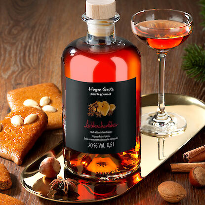 Flasche Lebkuchenlikör mit Glas, Gewürzen und Gebäck auf festlich gedecktem Tisch.