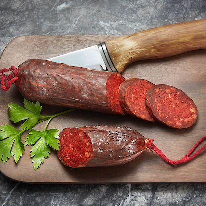 Aufgeschnittene Paprikasalami auf Holzbrett mit Messer und Petersilie.