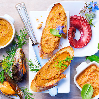 Meeresfrüchte-Pâté auf Baguettescheiben mit Muscheln, Oktopus und Kräutern angerichtet.