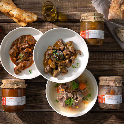 Drei Schalen mit Rindfleischgerichten samt passenden Gläsern, Brot und Olivenöl rustikal angerichtet.