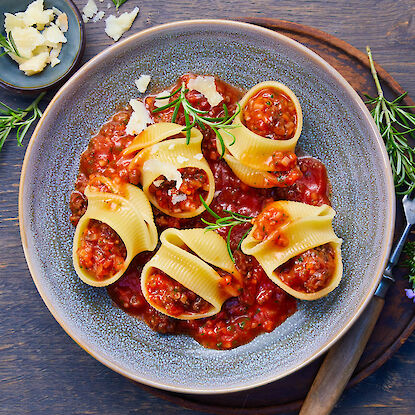 Gefüllte Muschel-Pasta in Tomatensauce mit Parmesan und Rosmarin auf grauem Teller angerichtet.