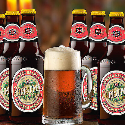 Mehrere Flaschen Shepherd Neame Christmas Ale mit einem frisch eingeschenkten Bierkrug voller Schaum im Vordergrund.