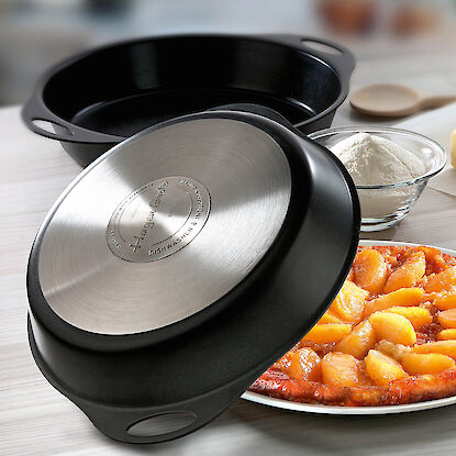 Gusseisenpfanne mit Edelstahlboden auf Tisch, daneben Zutaten und eine gestürzte Apfel-Tarte.