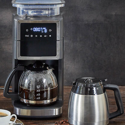 Filterkaffeemaschine mit Glaskanne, Thermoskanne und Kaffeebohnen auf Holztisch.