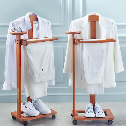 Zwei Kleiderst&auml;nder aus Holz mit wei&szlig;er Kleidung und Schuhen, jeweils mit Ablage f&uuml;r Accessoires und Rollen.